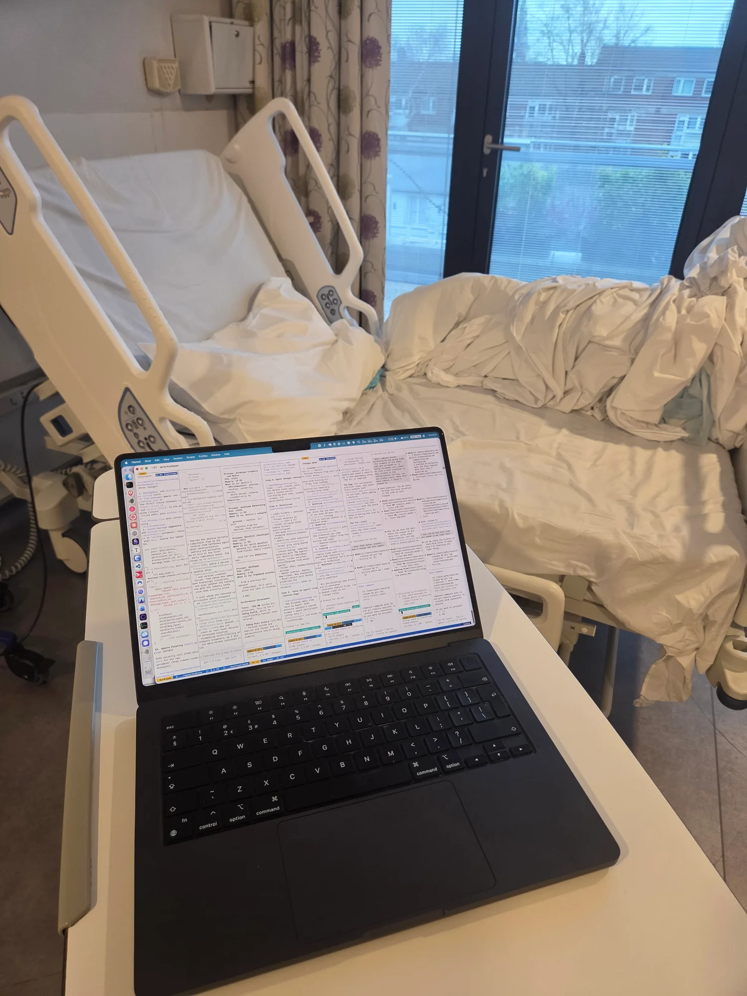 Laptop running Claude Code beside a hospital bed after surgery